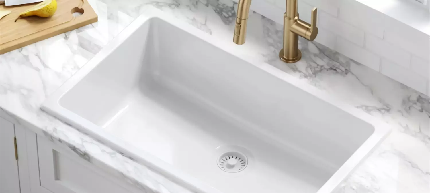 A kitchen sink installed in a marble countertop with a faucet nearby.