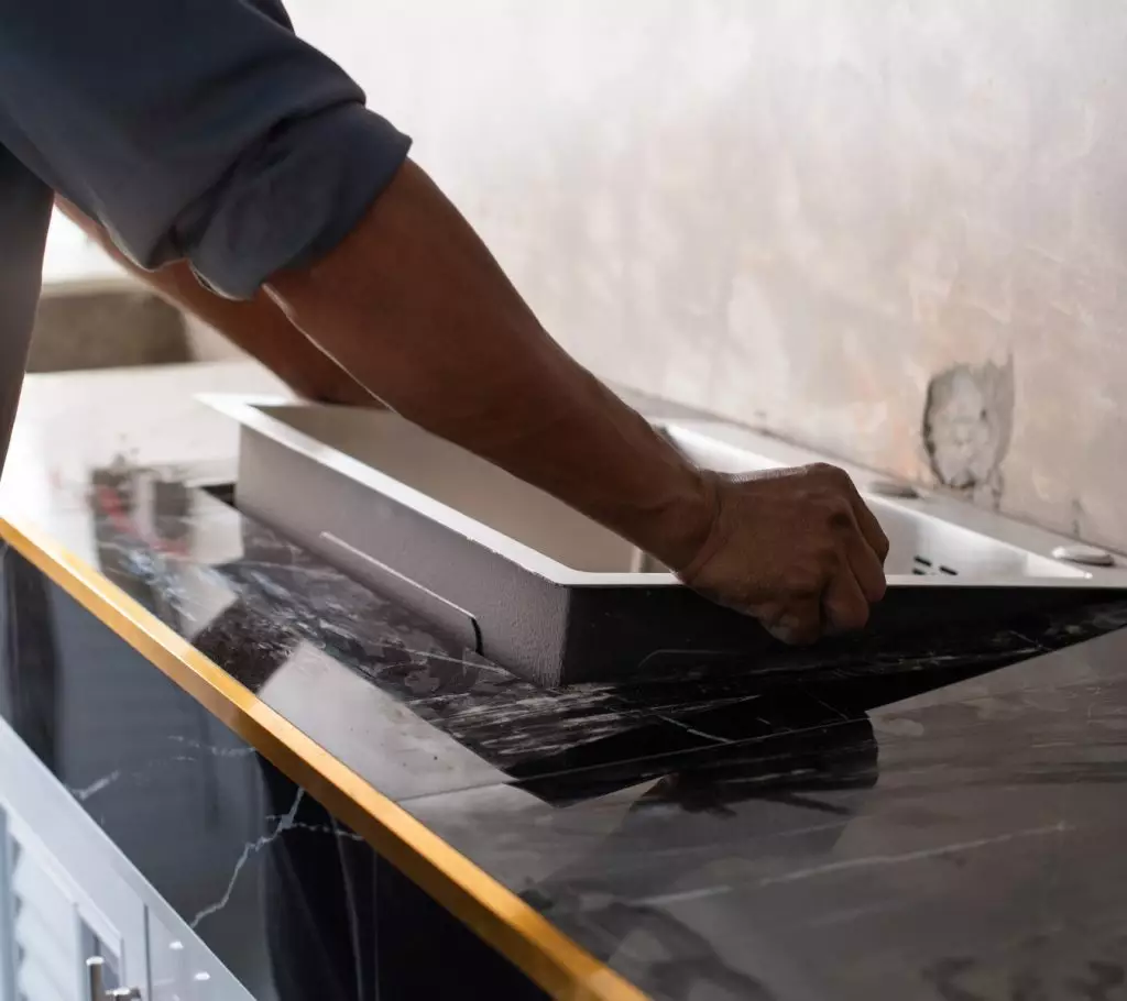 A person installing a kitchen sink into a countertop