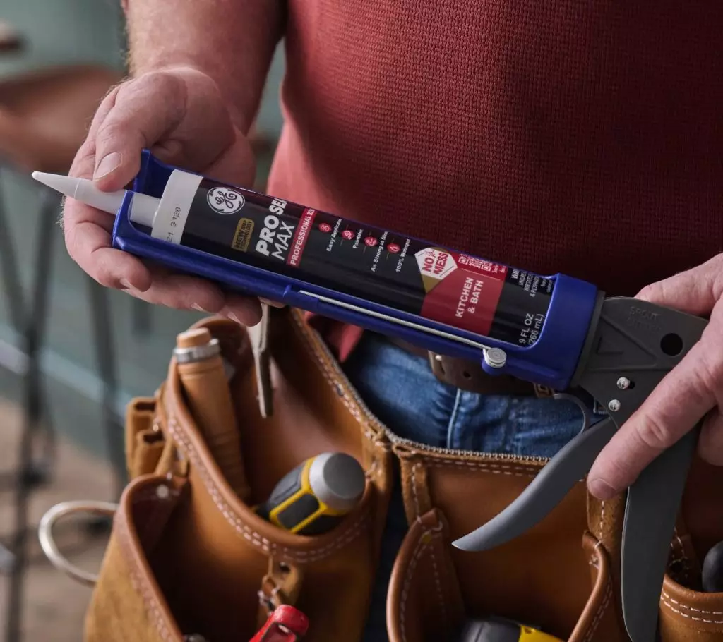 A person holding a caulking gun with a tube of GE Pro Seal Max Kitchen & Bath.
