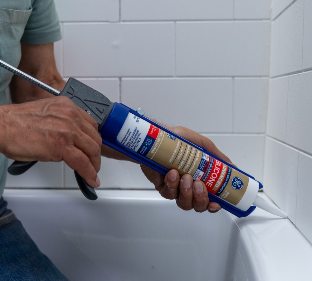 A person applying a waterproof sealant around a bathtub.
