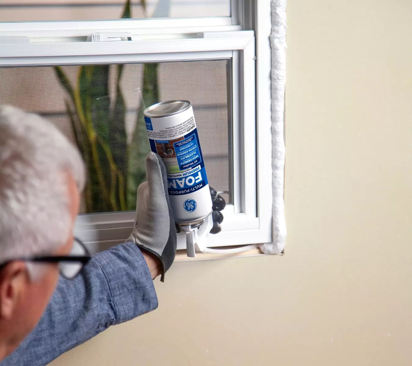 A photo of a homeowner applying insulation foam, wearing gloves.