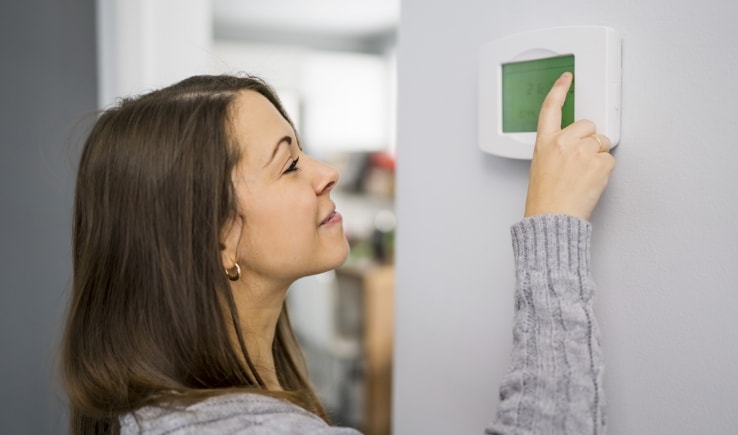 Photo of a woman adjusting a digital thermostat on the wall.