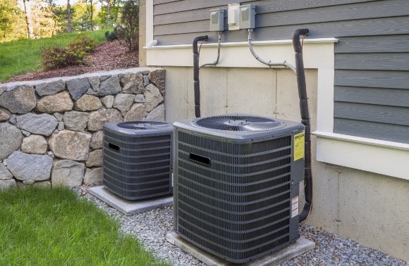 Photo of two HVAC outdoor units beside a house with stone and siding exterior.