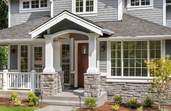 Photo of a modern house exterior with stone column details and multiple windows and a front door.