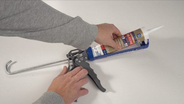 Photo of hands loading a caulk gun with a GE silicone sealant tube.