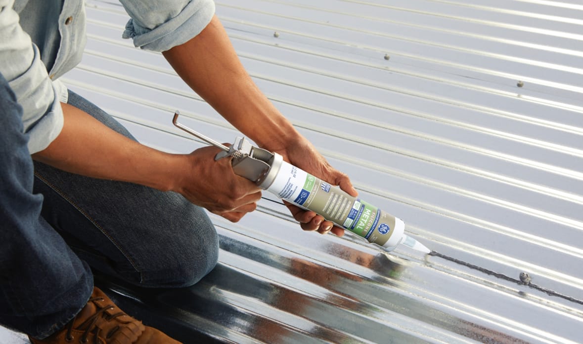 Photo of a person applying silicone sealant with a caulking gun on a metal roof.
