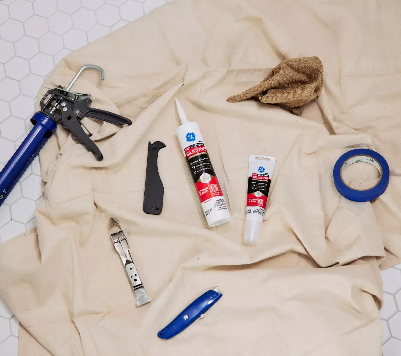 A photo of GE Supreme Silicone Kitchen & Bath, GE Sealant Remover tool, utility knife, tape, caulk gun and a cloth