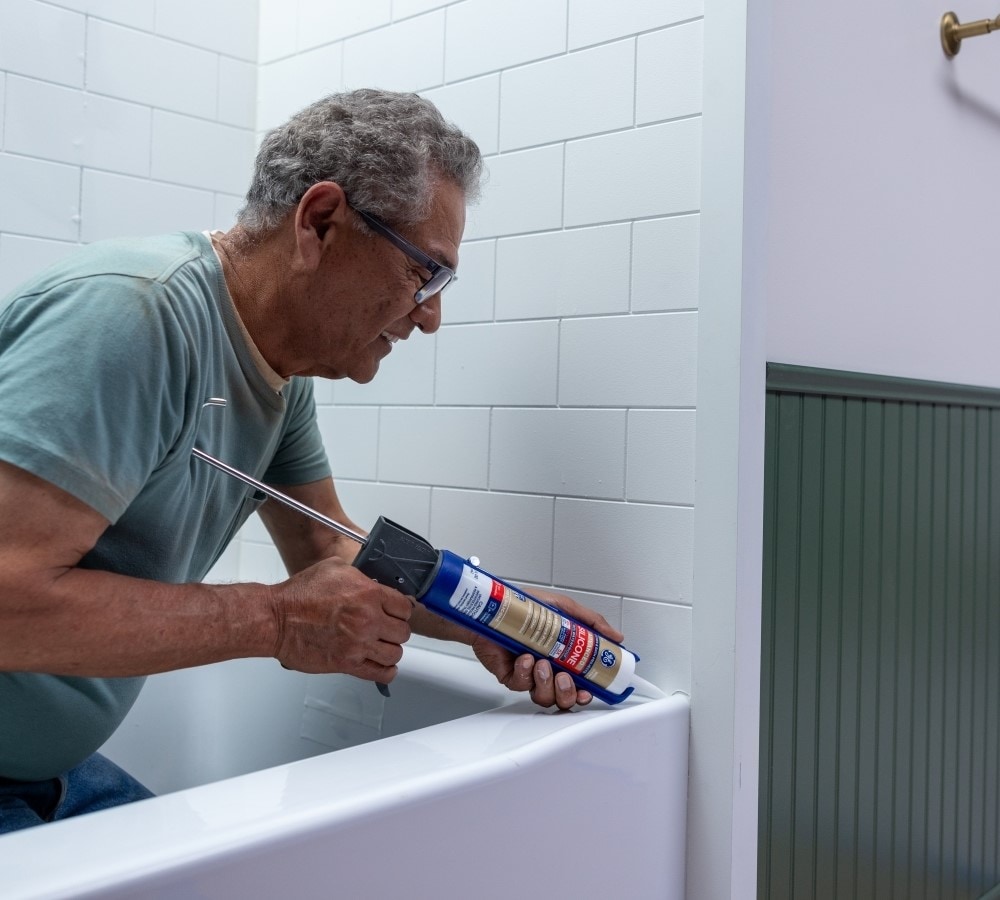 A tube of silicone sealant being applied to a bathtub.