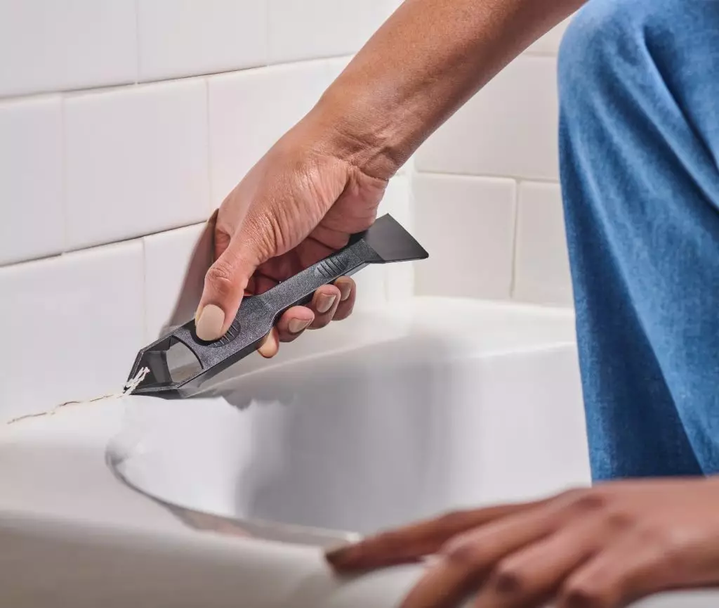A photo of a homeowner removing old sealant with the GE Sealant Remover Tool