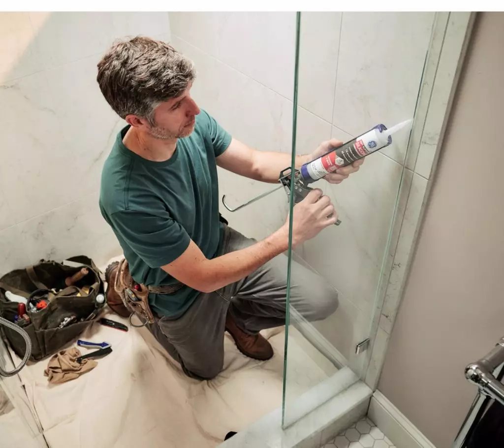 A photo of a homeowner applying sealant to a glass shower door
