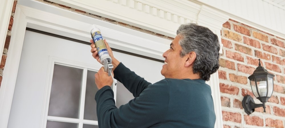 A homeowner applying sealant to a door frame.