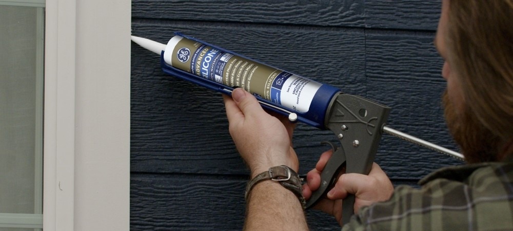 A man applies silicone sealant to a door frame.