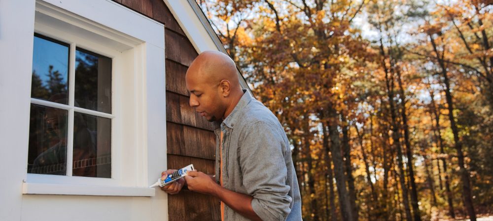 A photo of a homeowner applying sealant on an exterior window