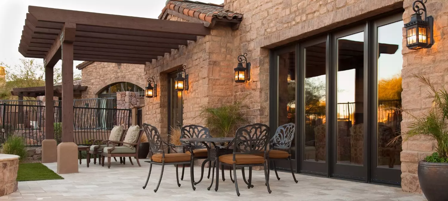 A stone home patio with dining furniture, a pergola and warm wall-mounted lantern lighting.