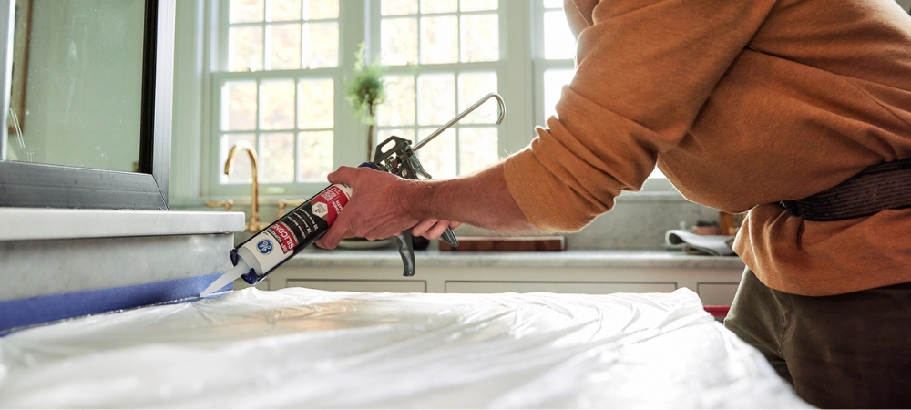 A person applying silicone sealant with a caulk gun.