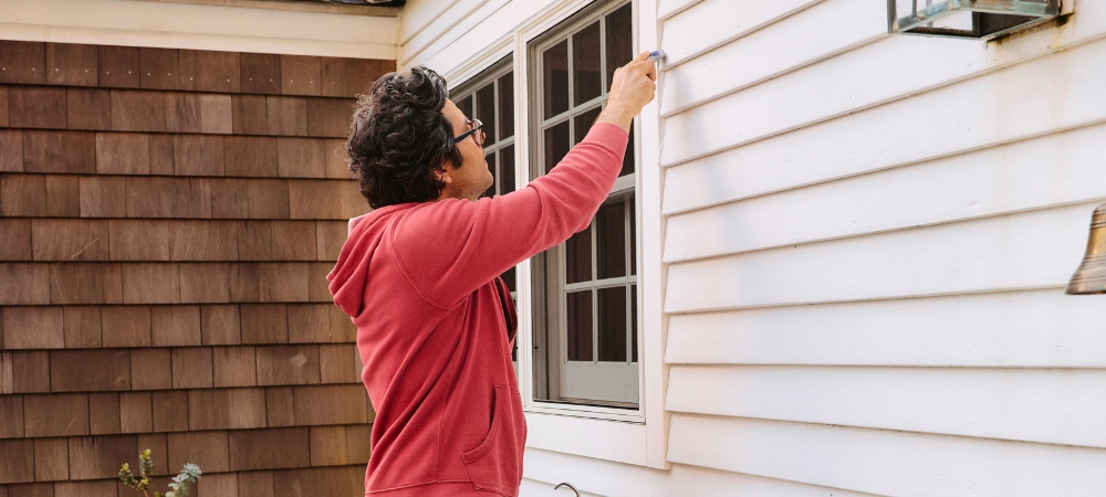 A homeowner inspects exterior window seals for damage.