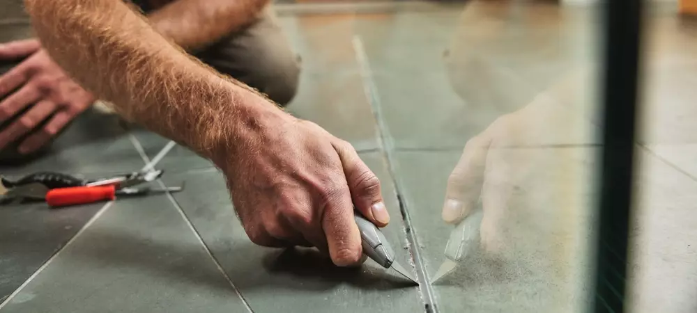 A homeowner removes old sealant from a glass shower pane