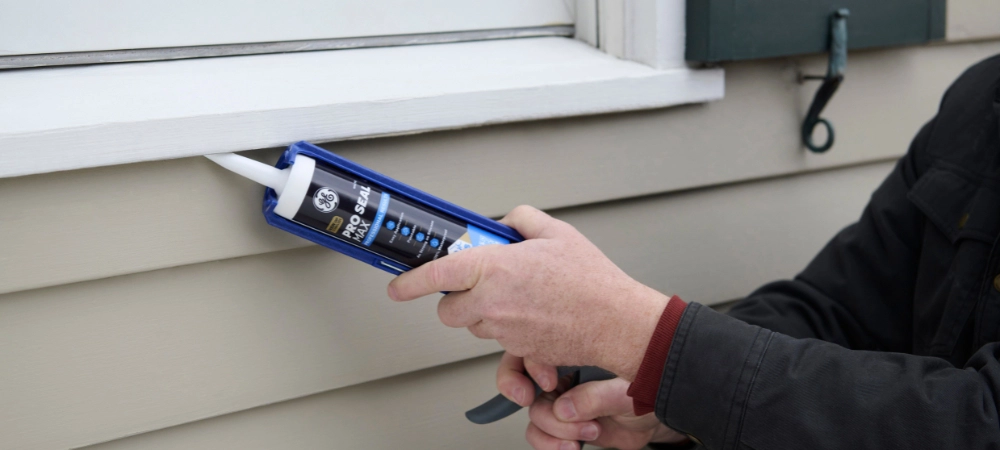 A person sealing exterior window trim with Pro Seal Max Window & Door sealant to prepare for the summer storm season.