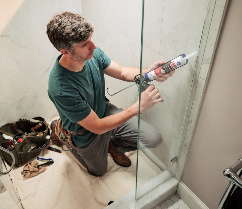 A photo of a homeowner applying GE Supreme Silicone Kitchen & Bath in a glass shower