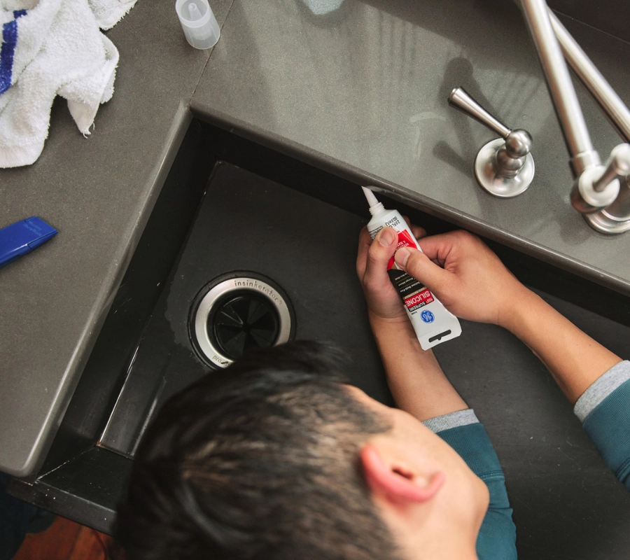 A person applying silicone sealant around a sink.