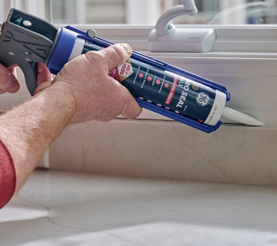 A man sealing a kitchen backsplash seam using GE Pro Seal Max Kitchen & Bath with a caulking gun.
