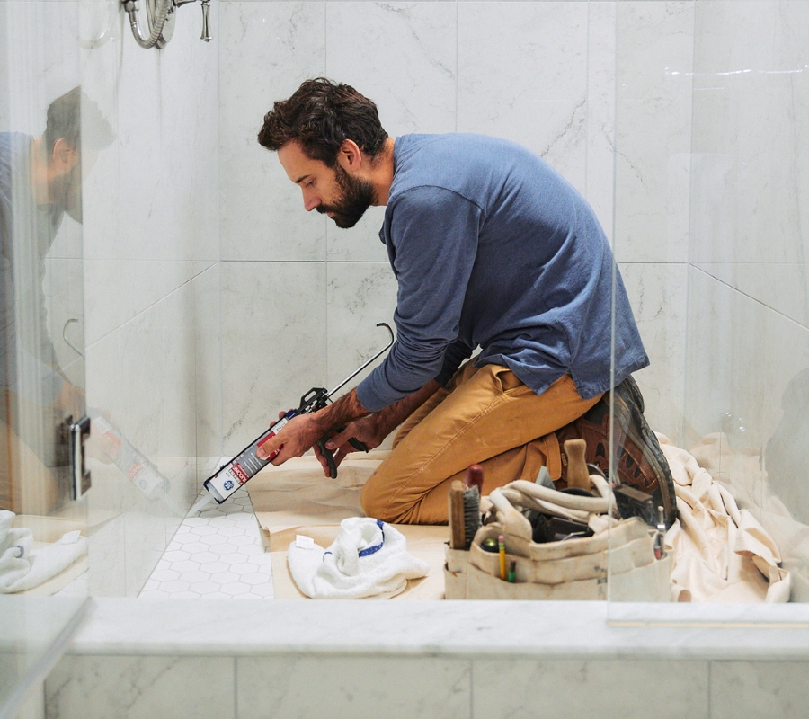 Person sealing bathroom tile with a silicone sealant.