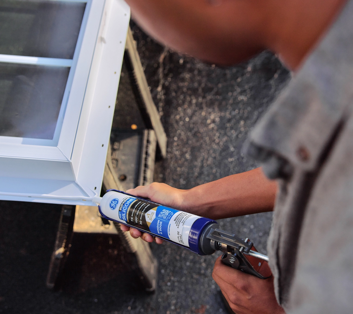 A homeowner using a caulking gun to apply GE silicone sealant to a vertical trim joint along siding.