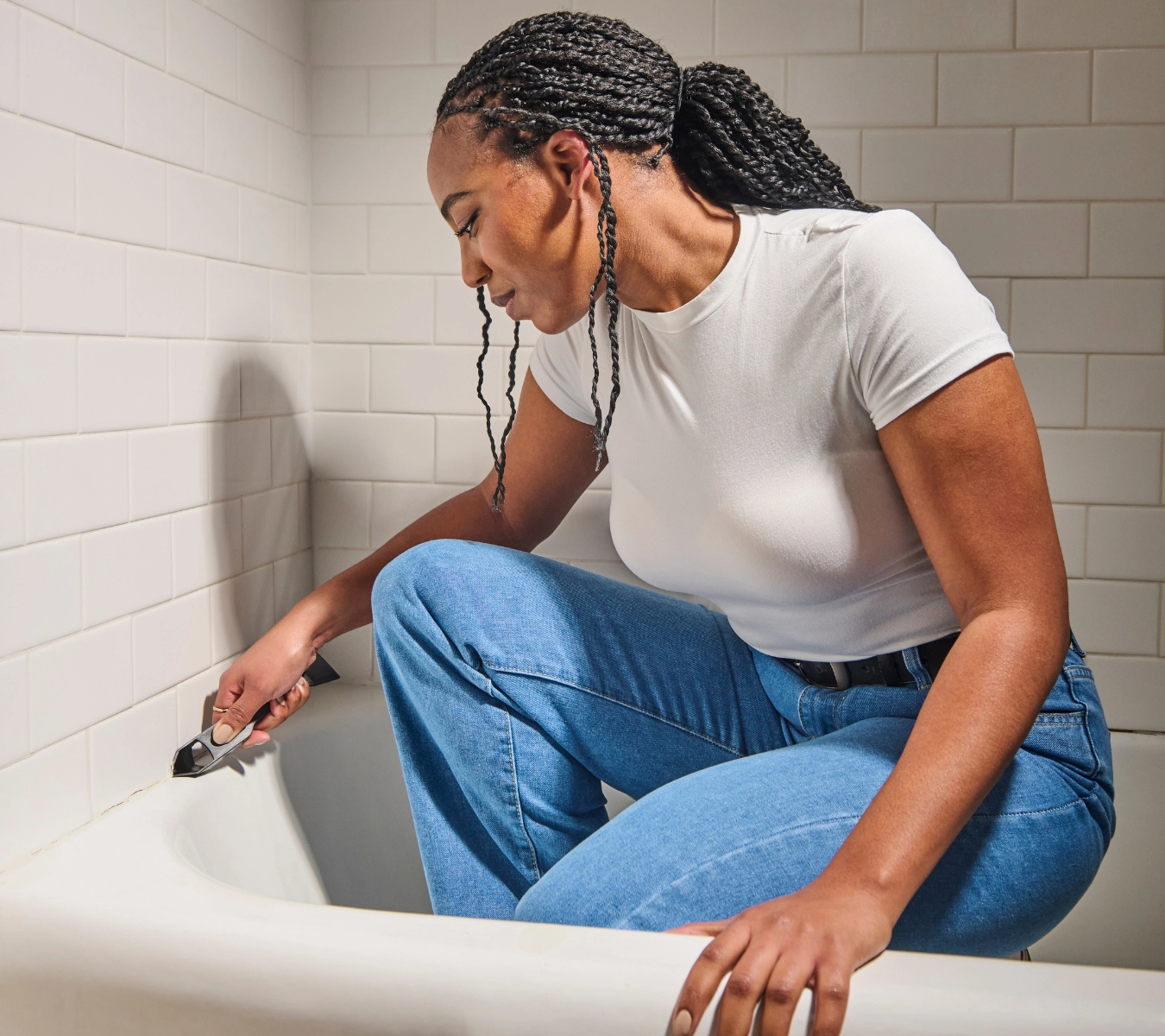 A homeowner removes old sealant in a bathroom with GE’s Sealant Remover Tool.