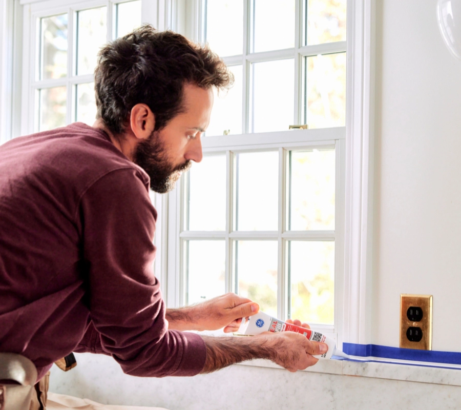 A photo of a homeowner sealing the backsplash in his kitchen using GE Seal & Fill Sealant.