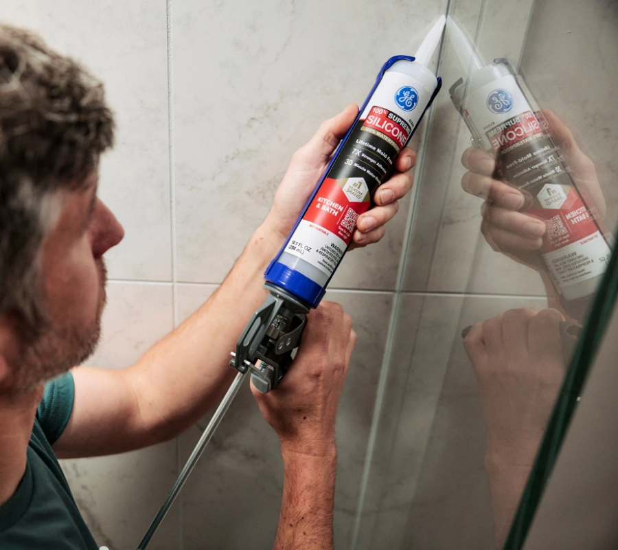 A person using a silicone sealant to seal a shower stall.