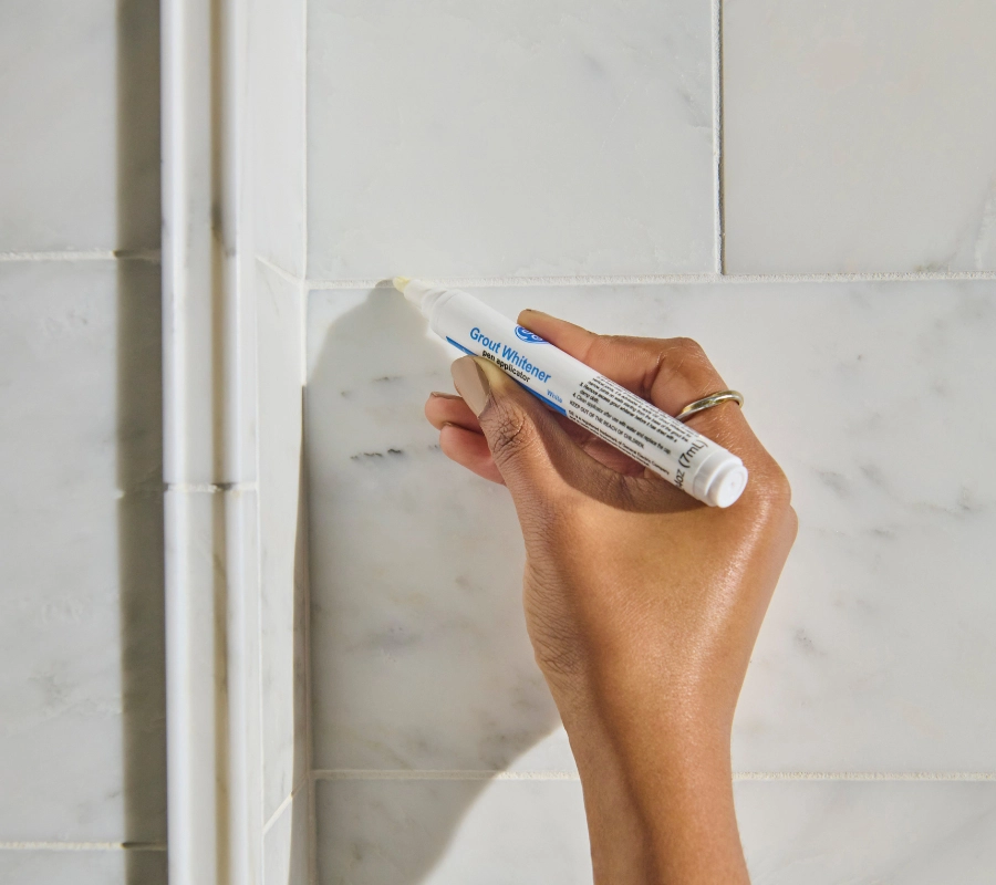 Someone whitening grout in a kitchen using GE’s new Grout Whitener Pen.