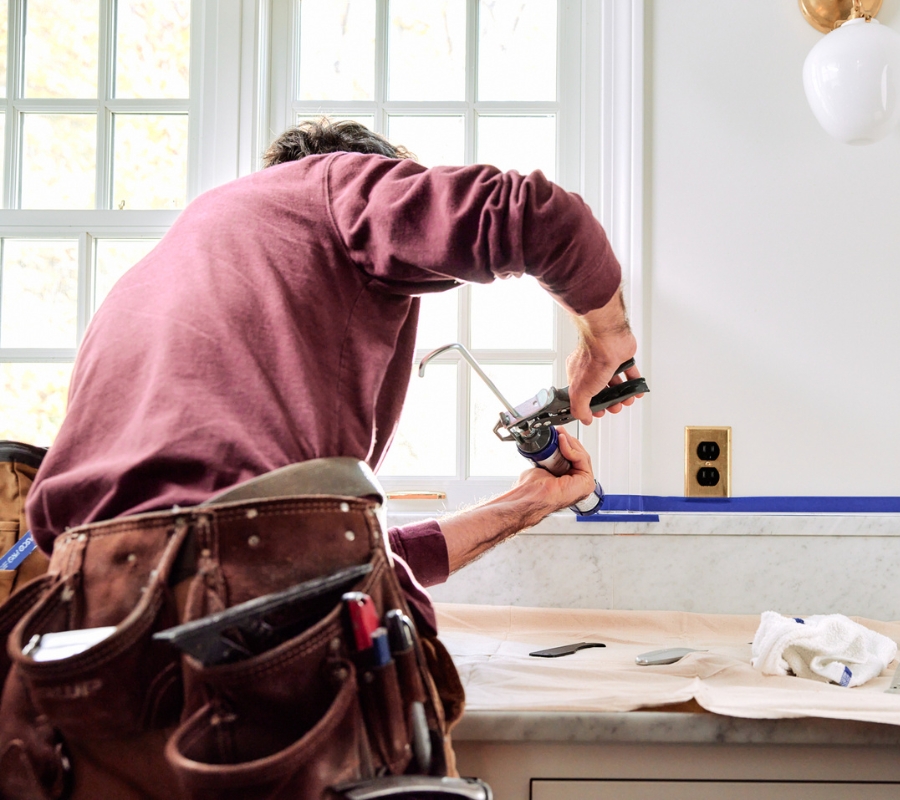 A homeowner sealing a kitchen backsplash.