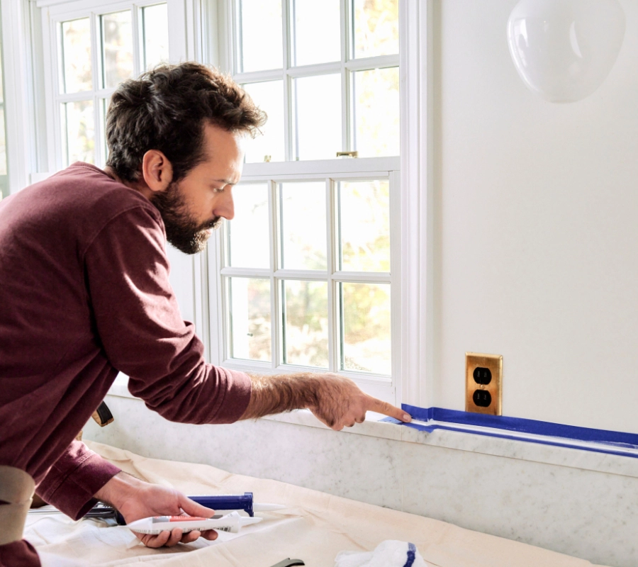 A photo of a homeowner using his finger to smooth a bead of sealant in the kitchen.