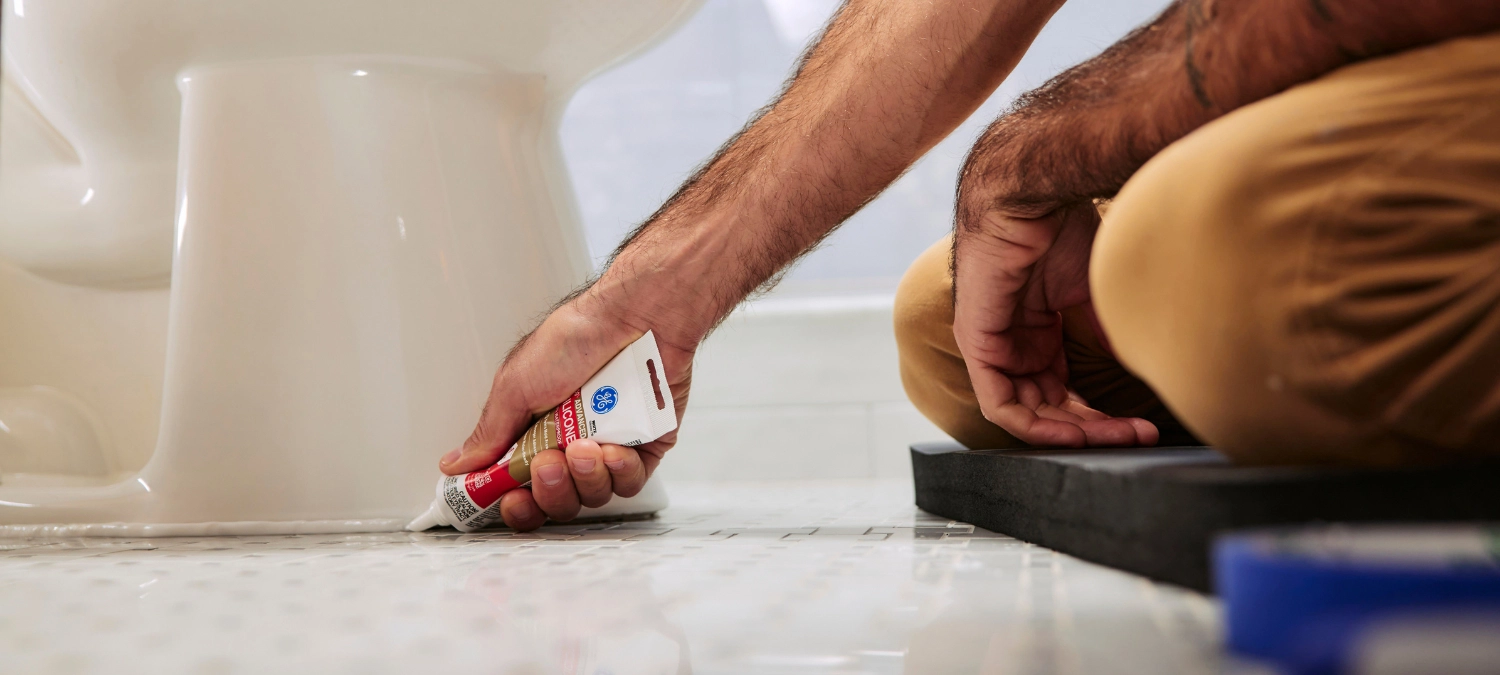A plumber applies silicone plumbing sealant to a bathroom fixture.