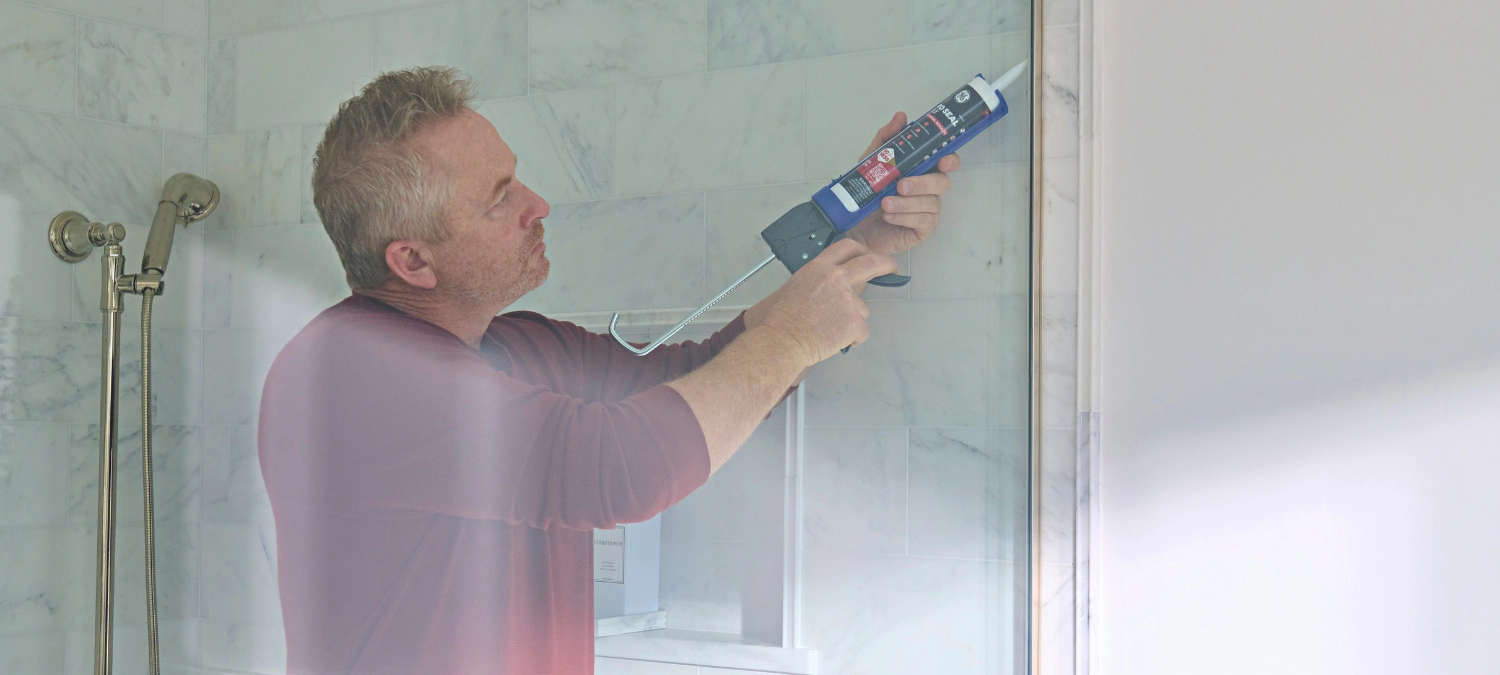 A person applying the best sealant for bathrooms around a shower in the home.