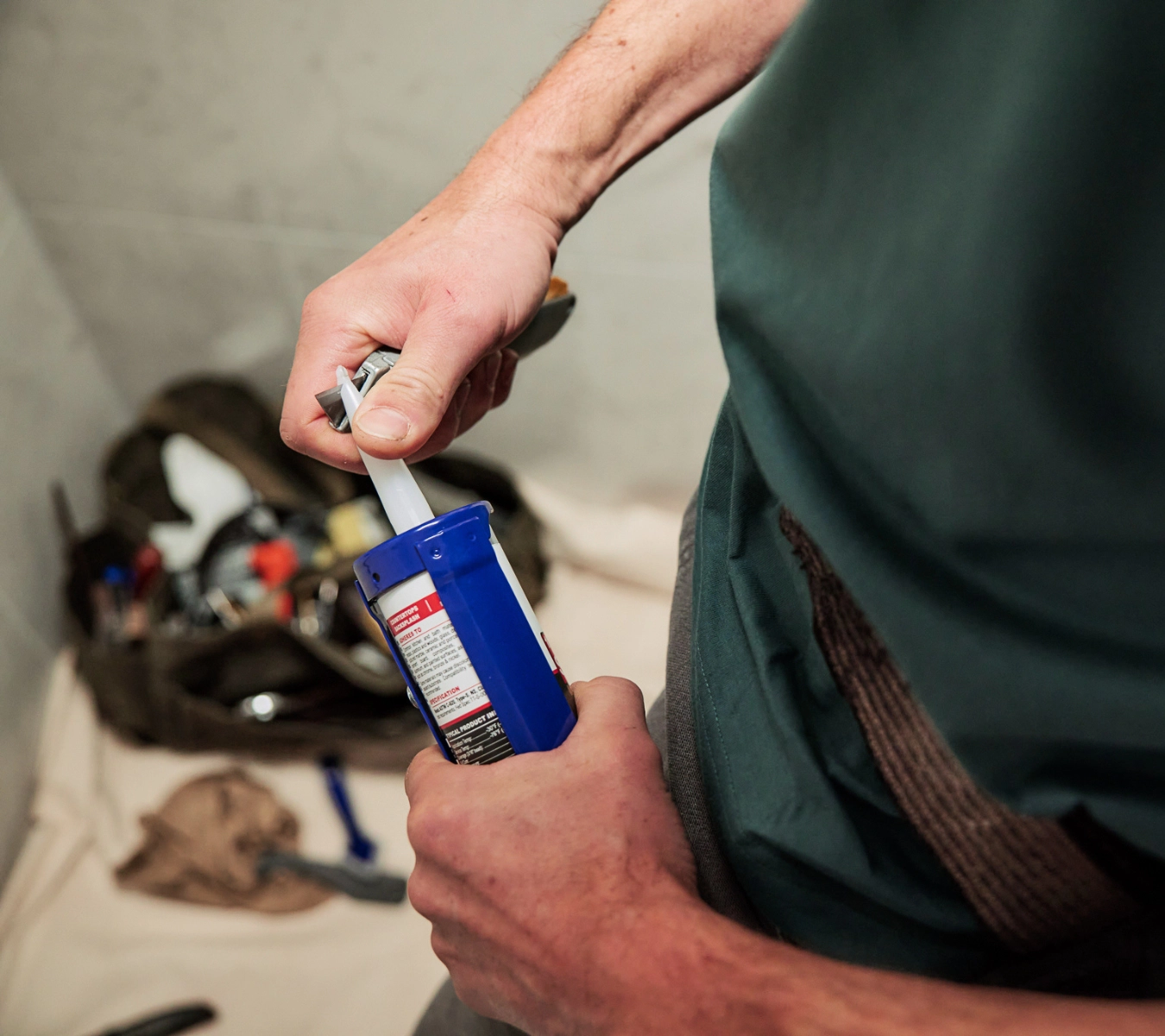 Cutting the nozzle of a GE silicone sealant tube at a 45-degree angle before sealing a bathroom fixture.