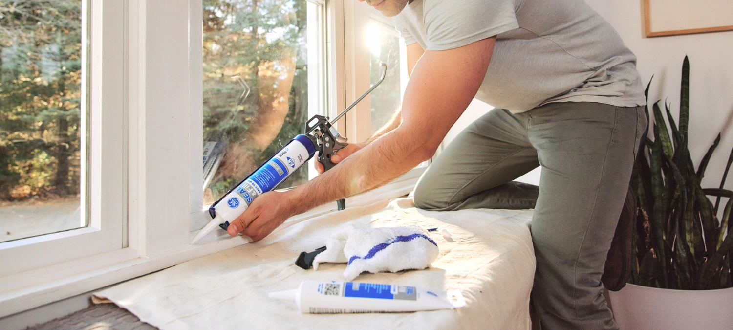 Person sealing kitchen windows and trim using a silicone sealant.