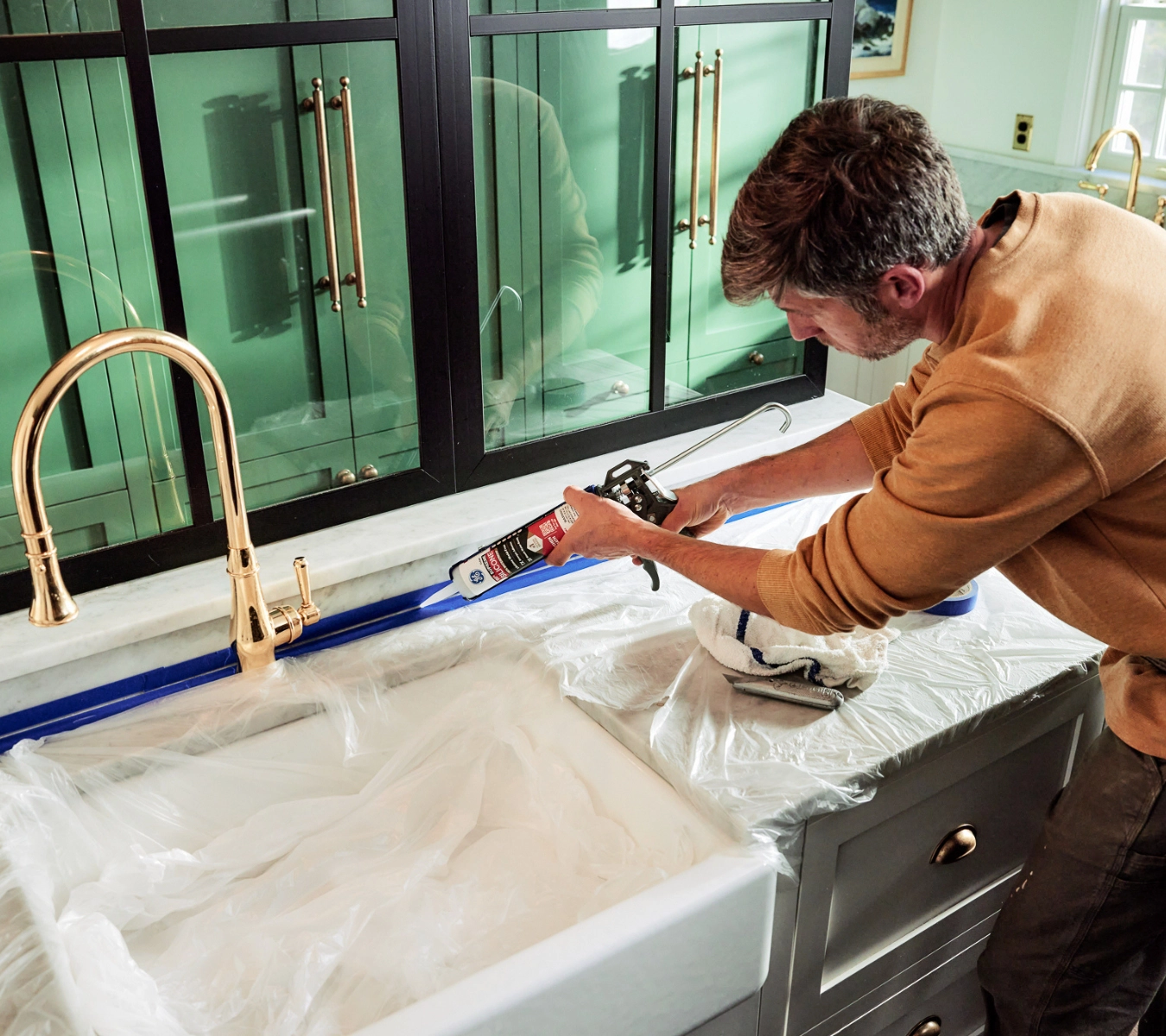 A person seals the edge of a kitchen backsplash with silicone sealant to prevent leaks.