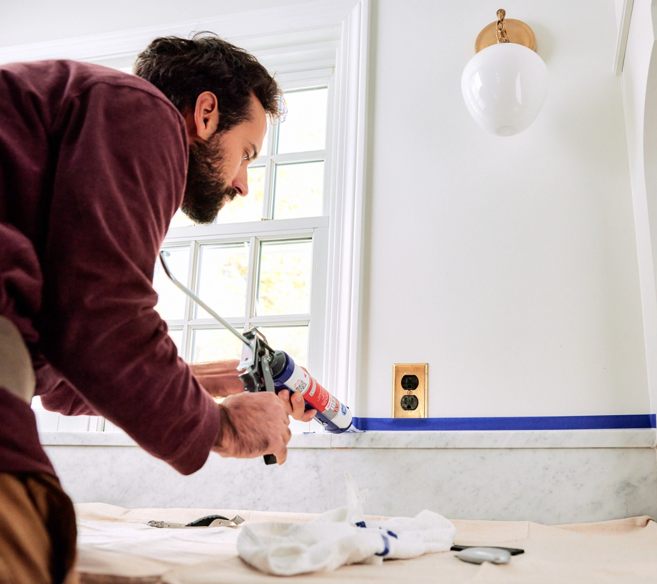 Person applying kitchen window sealant around a kitchen window.