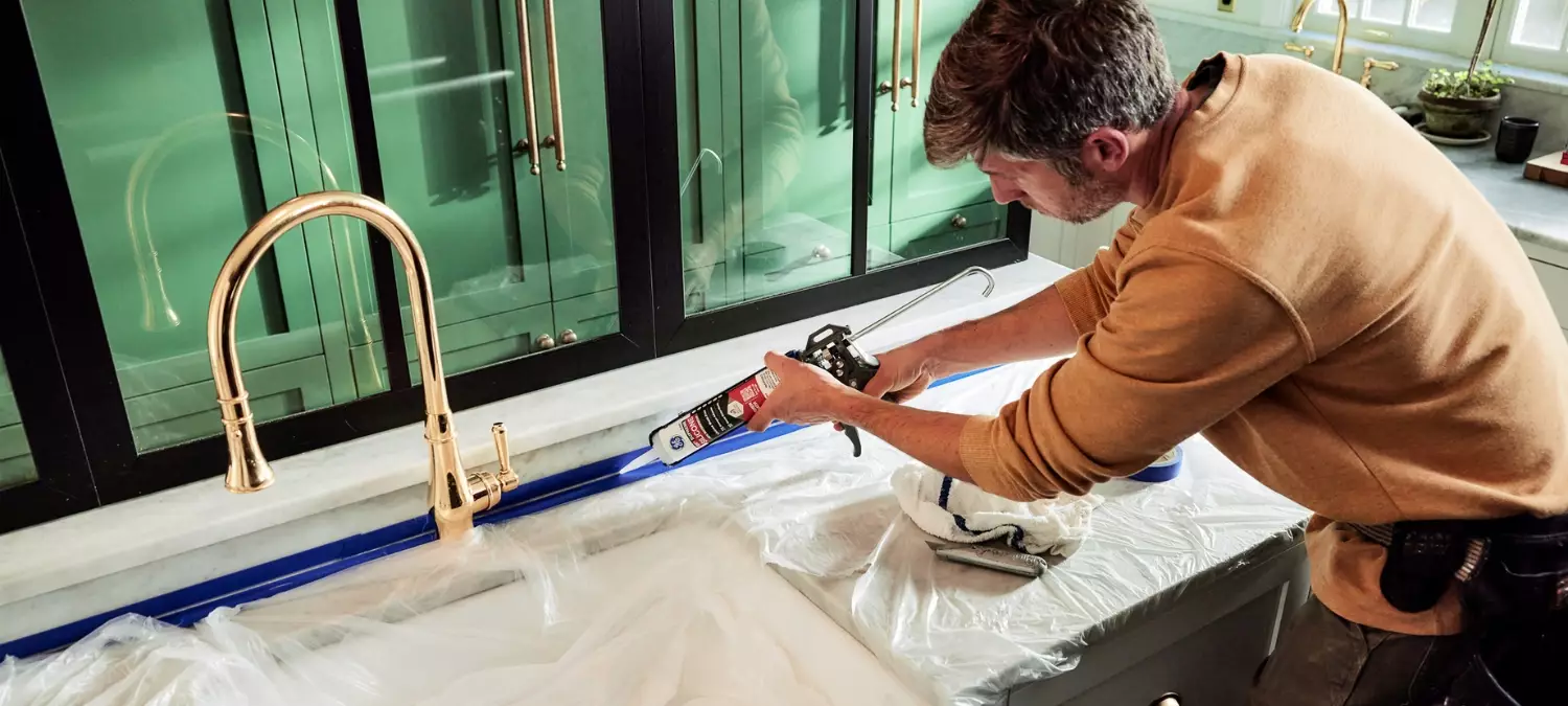 A photo of a homeowner sealing near their kitchen sink