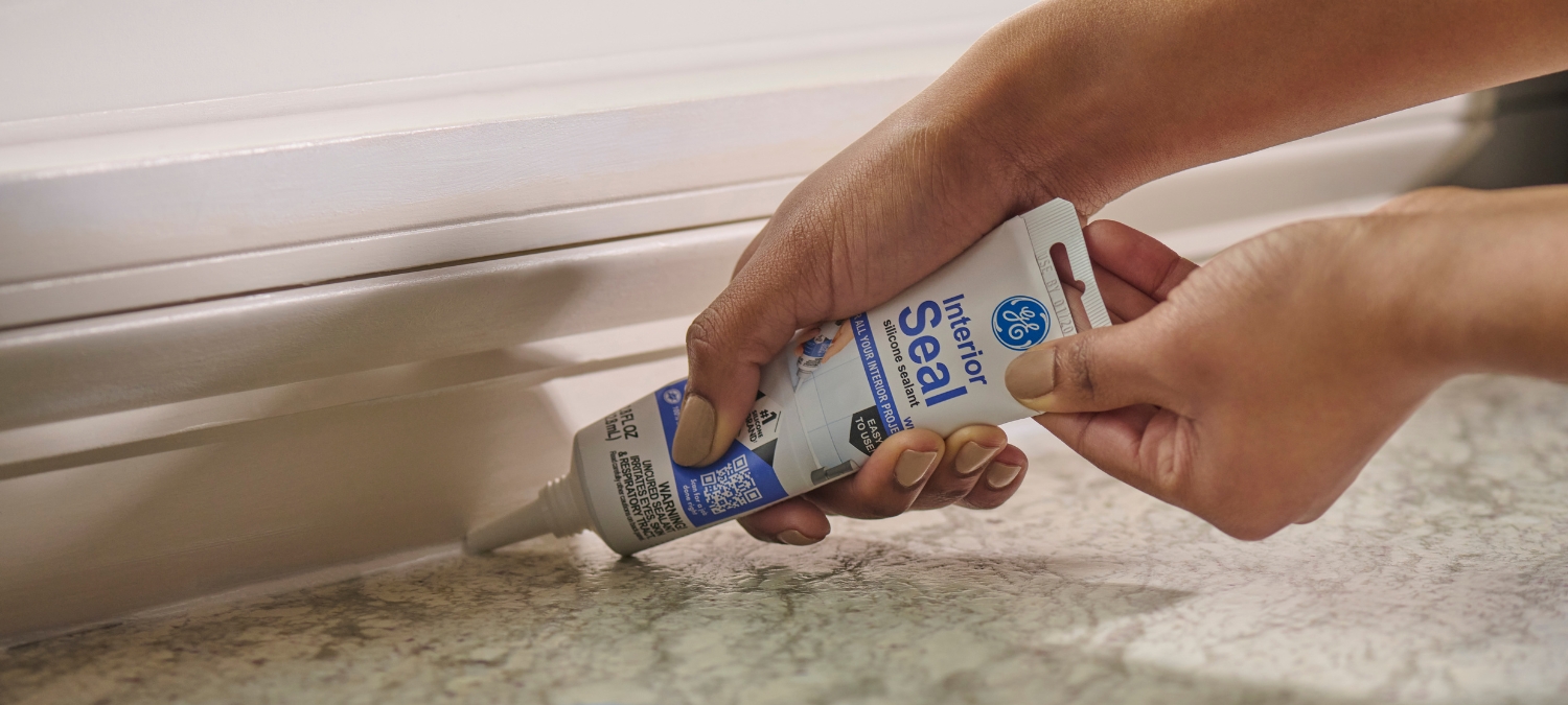 someone applying silicone sealant along a baseboard gap
