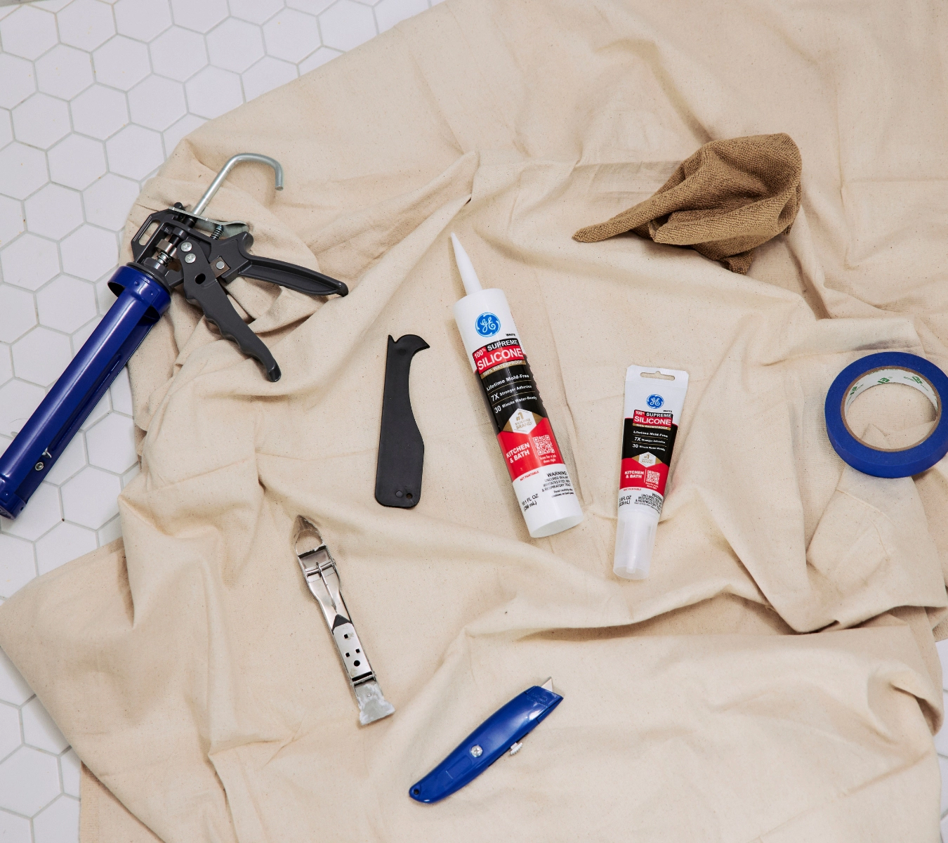 A top-down shot of essential sealing tools arranged on a drop cloth over a tiled floor. 