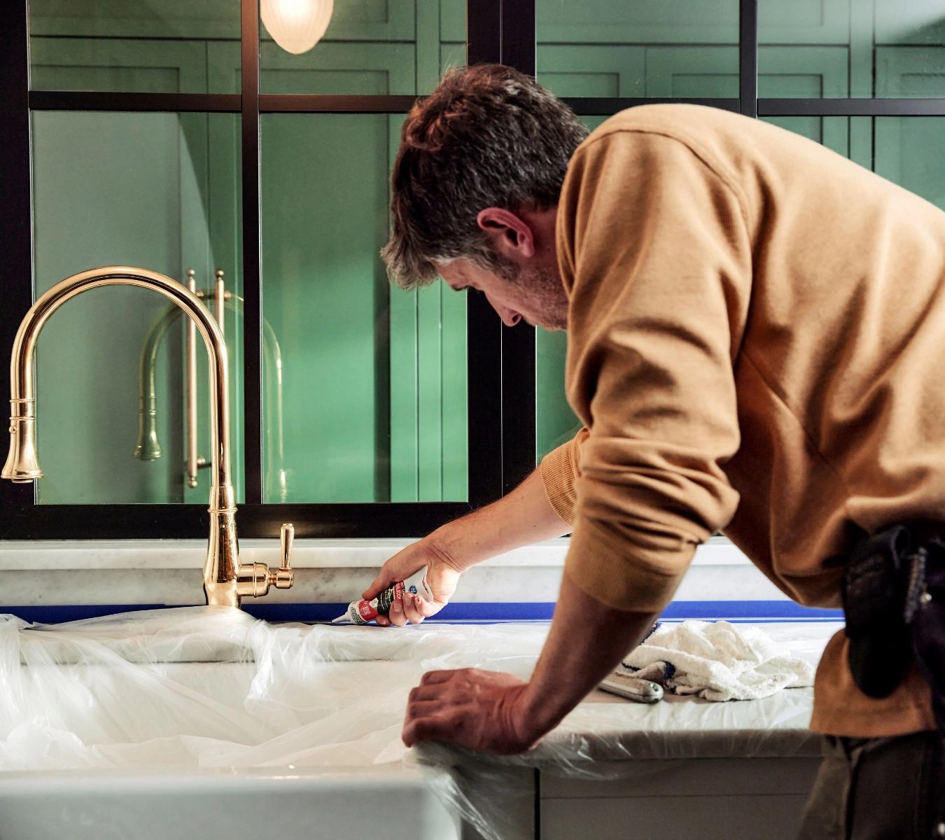 A man using GE Supreme Silicone Kitchen & Bath Sealant (squeeze tube) to apply a clean bead along the kitchen sink backsplash seam. 