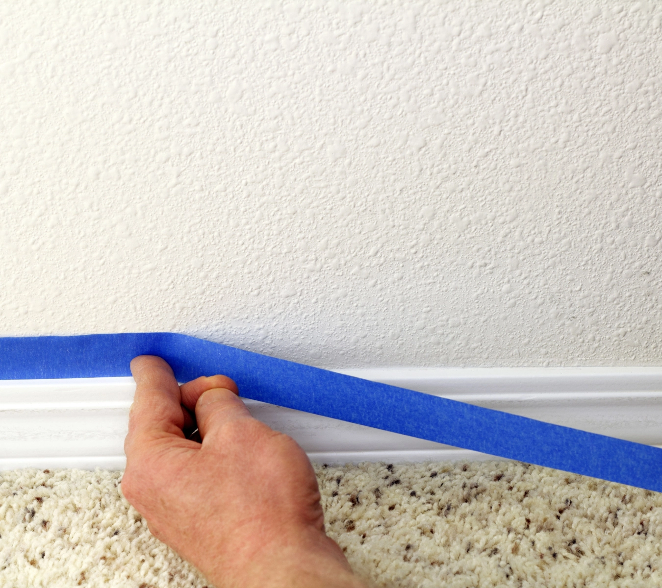 A photo of a homeowner applying painter’s tape along baseboards.