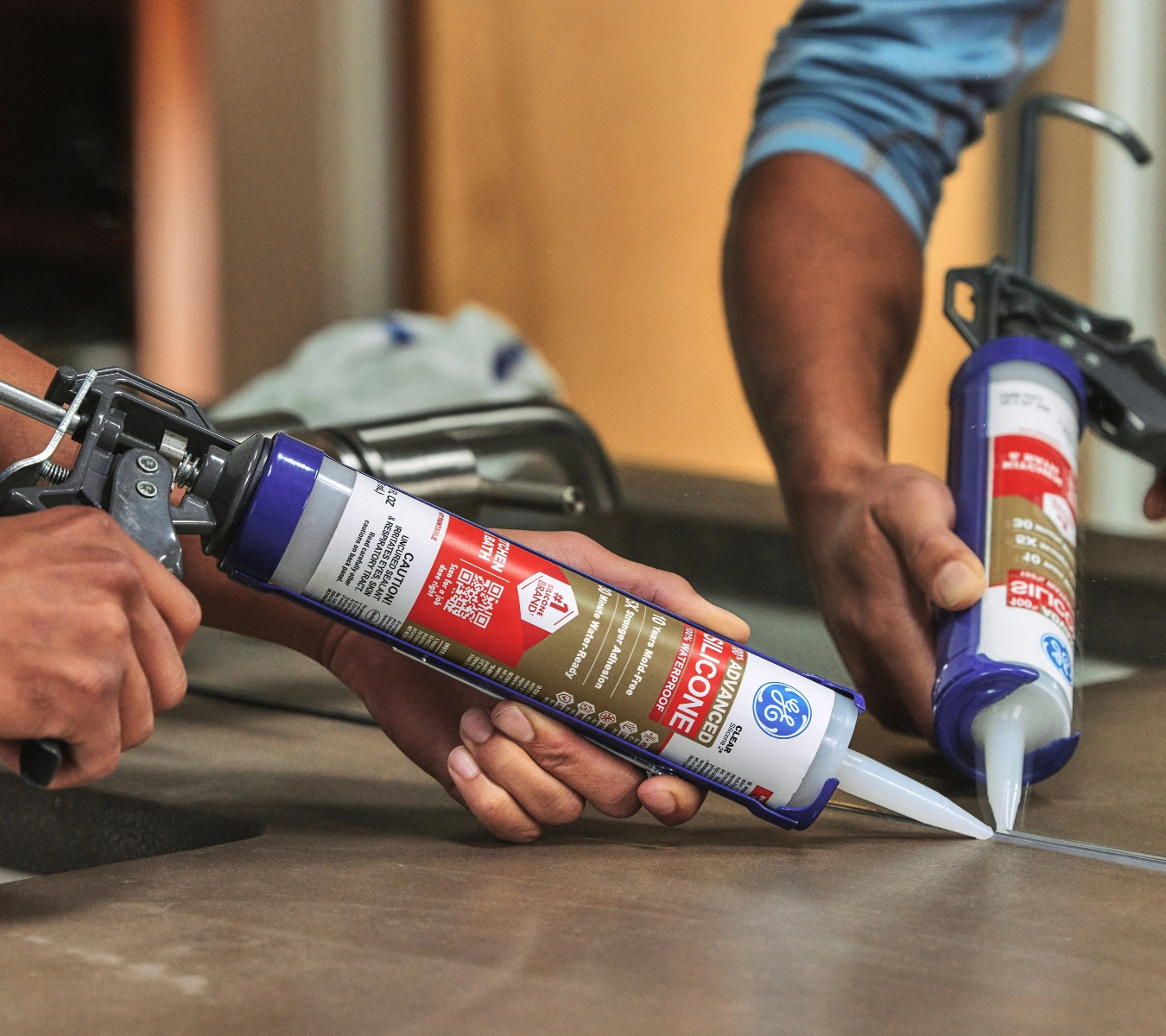 A contractor applying GE Advanced Silicone Kitchen & Bath Sealant along a glass panel and tile joint.