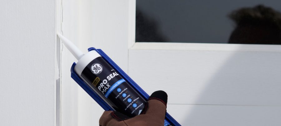 1 Homeowner using a caulk gun to seal around a drafty window frame with GE Pro Seal Max Window Door. Clear cartridge branding e1772569839382