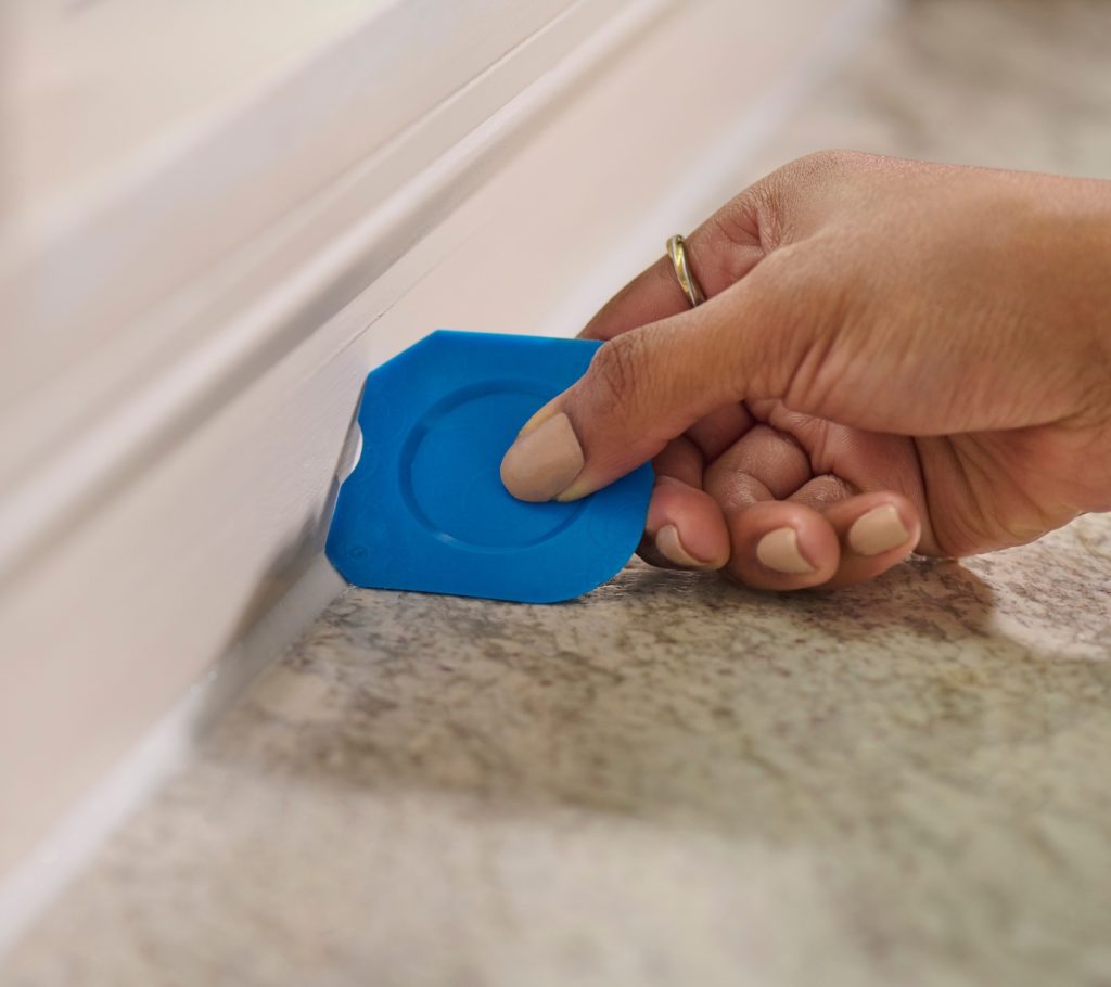 A person using the GE Sealant Smoothing Tool to create a watertight silicone seal along a countertop.