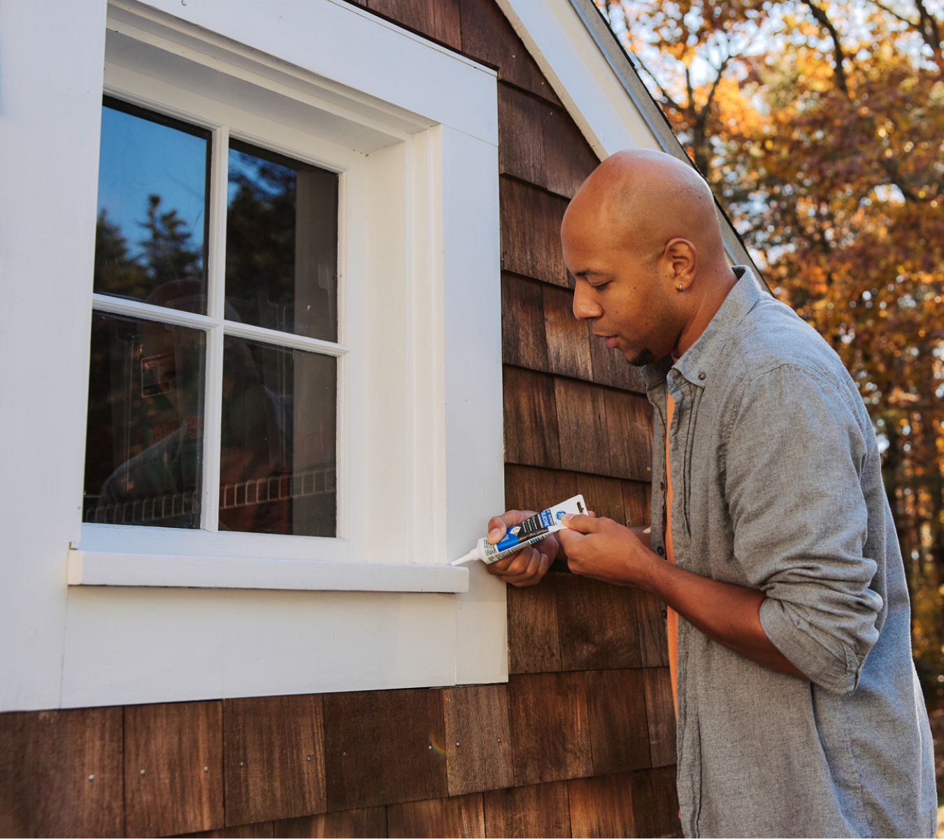 Property maintenance worker applying GE Supreme Silicone Window & Door around an exterior window frame to stop water intrusion.