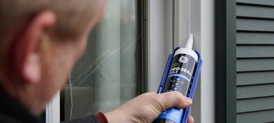 Homeowner sealing a window frame with GE Pro Seal Max Window & Door on a winter day to protect the home from winter drafts and moisture.