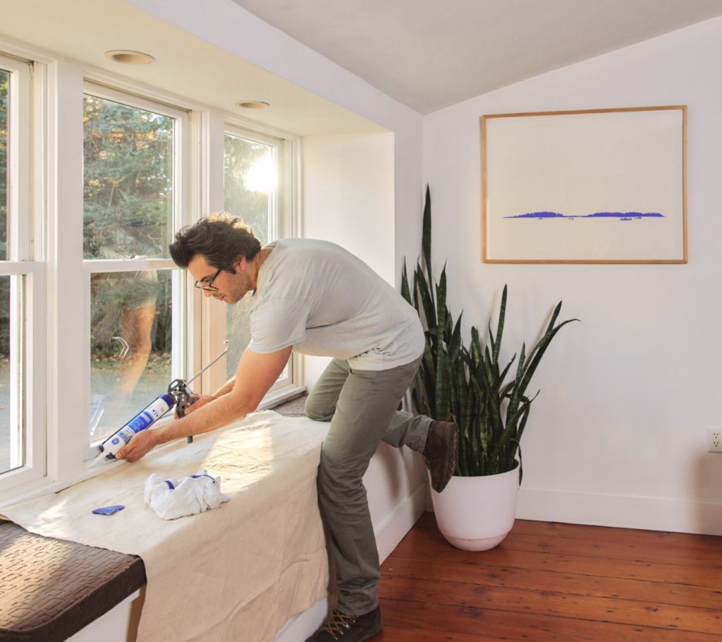 Applying a GE sealant along a window frame for winter protection.